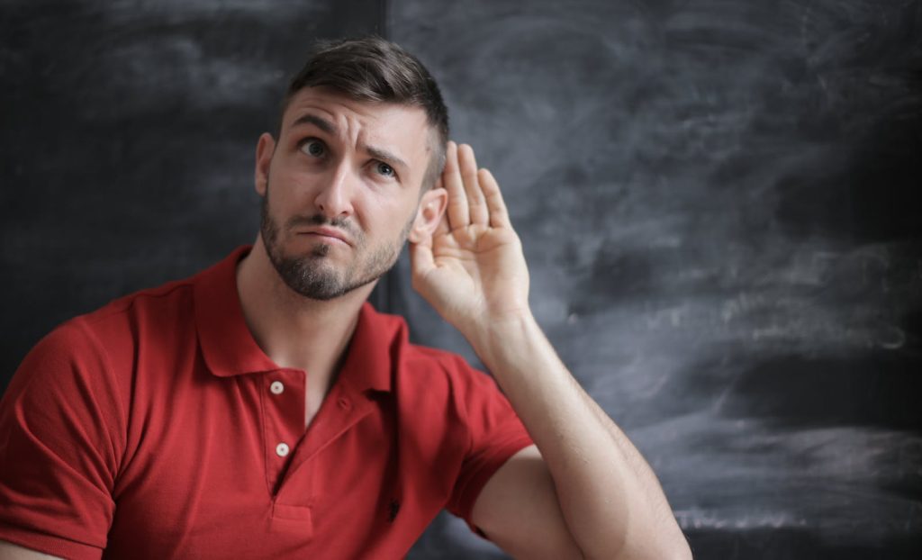 Un homme pensif écoute attentivement sur un fond de tableau noir dans un polo rouge.